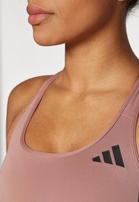 Roza sportska majica bez rukava s izrezom u obliku scoop neckline i tankim naramenicama. Crni logotip na lijevoj strani. Glatka, rastezljiva tekstura tkanine.
