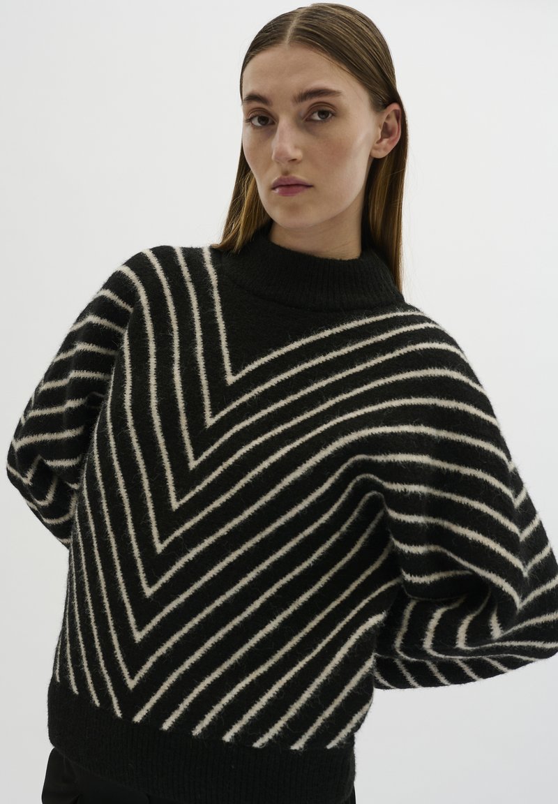 Maglione a righe bianco e nero con colletto alto a coste, caratterizzato da un motivo a zigzag e maniche oversize in una texture morbida.