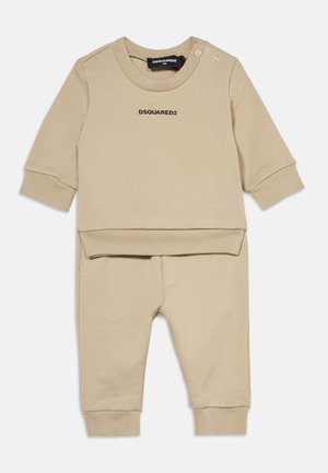 Beige babyoutfit-sæt med langærmet top med teksten "DSQUARED2" og matchende bukser, begge med ribmanchetter, lagt fladt.