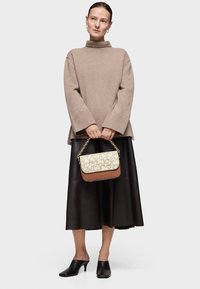 Beżowy, oversize'owy sweter sutkowy z wysokim kołnierzem, zestawiony z czarną skórzaną spódnicą. Brązowa i kremowa torebka typu crossbody z geometrycznym wzorem. Czarne klapki.