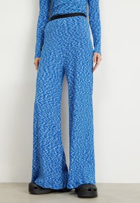 Blue wide-leg pants in a textured, patterned fabric with swirls of different blues. Features a black waistband. Paired with black footwear.