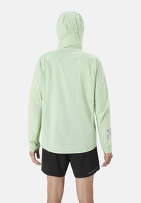 Hellgrüne, langärmelige Jacke mit Kapuze aus leichtem Material. Verfügt über reflektierende Akzente an den Ärmeln und Text auf der Rückseite.