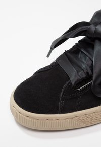 Gros plan d'une basket en daim noir avec une semelle épaisse beige et des lacets larges en ruban de satin noir noués en nœud.