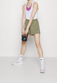 Nike urheiluasut: valkoinen verkkomaisesta kankaasta valmistettu tankkitoppi, violetti urheiluliivi, oliivinvihreät shortsit. Musta kahvakuula, vaaleanpunaiset urheilukengät, valkoiset sukat mustalla logolla.