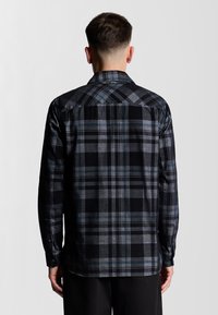 Camisa de cuadros en negro y gris con mangas largas, puños abotonados y un cuello clásico, que muestra una tela tejida texturada con un ajuste entallado.