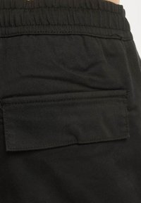Svarte shorts i stoff med tekstur, med elastisk midje og en baklomme med klaff.