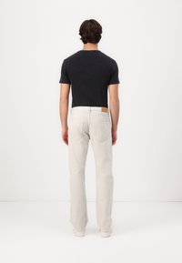 Camisa negra de manga corta combinada con jeans rectos beige claros. Los detalles destacados incluyen una etiqueta de cuero en la cintura y una textura de tela suave.