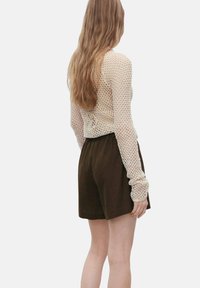 Lichtbeige gebreid langemouwtop met open gaaspatroon, gecombineerd met donkerbruine hoge taille shorts.