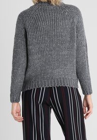 Pull gris en tricot avec un motif texturé, manches raglan et ourlet côtelé. Assorti à un pantalon à rayures noires et blanches.