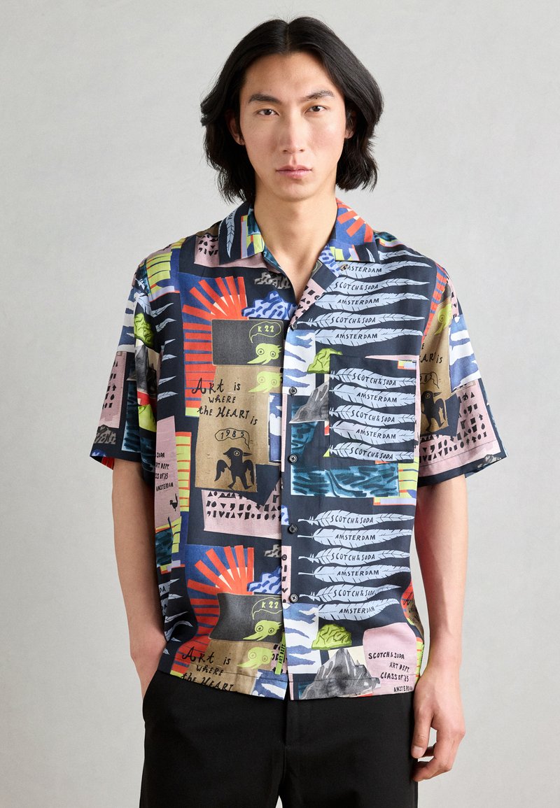 Short-sleeve button-up shirt in a multicolored pattern, featuring various prints, including text and graphics in vibrant hues on a dark background.