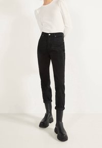 Vaqueros de mezclilla negros de talle alto con pierna estrechada, puños enrollados y textura sutil, combinados con botines negros de plataforma.