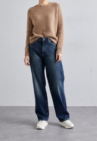 Suéter beige esponjoso combinado con jeans oscuros de corte ancho y zapatillas blancas. Diseño sencillo con puños acanalados y un ligero desvanecimiento en los jeans.