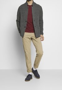 Szarawy sweter o fakturze dzianiny, bordowy t-shirt, beżowe spodnie chino oraz ciemnoniebieskie zamszowe buty z białymi skarpetkami. Codzienny strój z rozpiętą kurtką na guziki.