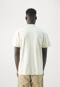 Camiseta de manga corta, color crema, en una tela suave con un corte relajado, que presenta un cuello simple y un dobladillo recto.