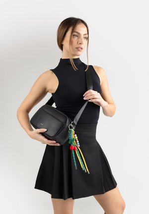 Donna con top nero senza maniche e gonna che tiene una borsa a tracolla nera con accessorio colorato di nappine di perline.