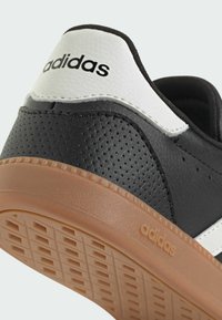 Čierne tenisky s perforovanou textúrou, biele akcenty na päte a strane a karamelová gumová podrážka so štvorcovým vzorom a logom.