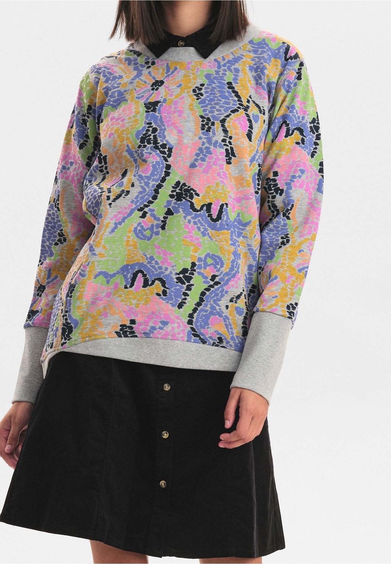 Flerfärgad sweatshirt med ett livfullt abstrakt mönster i rosa, lila, grönt och gult, med grå muddar och nederkant. Matchas med en svart kjol.