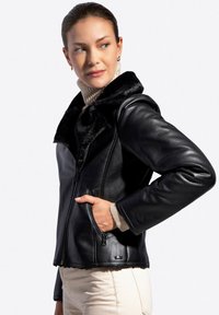Czarna skórzana kurtka z sztucznym futerkiem przy kołnierzu, zamek błyskawiczny i kieszenie boczne. Charakteryzuje się eleganckim designem i gładką fakturą dla nowoczesnego wyglądu.
