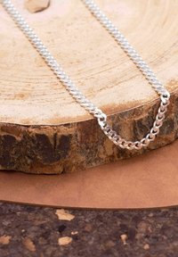 Collier en chaîne en argent avec des maillons entrelacés, présenté sur un fond de tranche de bois, mettant en valeur une finition poli et une texture lisse.