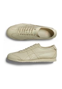 Beige Leder-Sneaker mit niedrigem Profil, strukturiertem Gummisole und Schnürdesign. Enthält tonale Markenlogos und subtile Stickdetails.