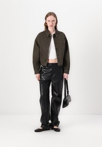 Giacca di jeans cropped verde oliva, top cropped bianco, pantaloni a gamba larga in pelle nera, ballerine nere e una piccola borsa nera a tracolla.
