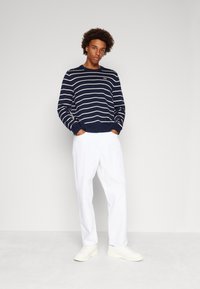 Marine gestreepte trui met witte strepen, ronde hals, ribbelboorden en onderrand, gecombineerd met witte losse broek en witte schoenen.