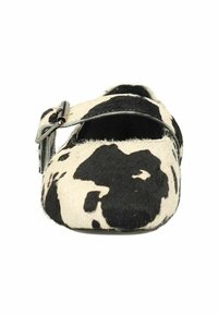 Chaussure plate Mary Jane en peau de vache noire et blanche avec une bride et une boucle argentée, dotée d'une surface texturée et d'une forme à bout rond.