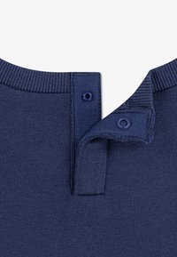 Granatowa dzianinowa koszulka polo z zapięciem na guziki przy kołnierzyku. Posiada delikatną teksturę oraz prążkowany dekolt. Dwa zatrzaski przy kołnierzu.