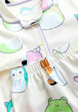 Pijamas crème pour enfants avec col et boutons, ornés d'imprimés d'animaux colorés incluant des grenouilles, des hiboux et un chat avec une corne.