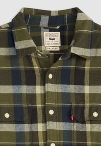 Geruite flanellen shirt in groen, marineblauw en crème, met een ontspannen kraag, knoopsluiting en een borstzak met een rood label.