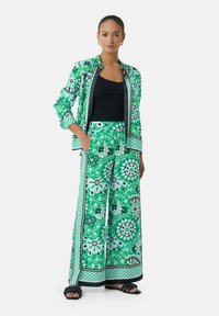 Jacke und weite Hose im floralen Muster in Grün, mit kontrastierendem schwarzen Trim und lockerer Passform, aus leichtem Stoff gefertigt.