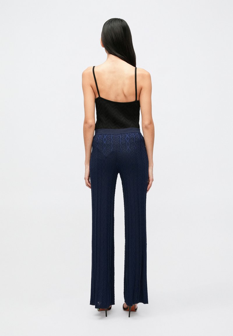 Camisole nera testurizzata con spalline sottili abbinata a pantaloni svasati a vita alta di colore blu navy con motivo, caratterizzati da una trama a coste e da una cintura elastica.