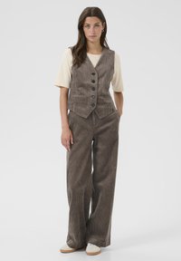 Bruine corduroy gilet met zes knopen, gecombineerd met bijpassende brede broek en een crèmekleurig crewneck t-shirt, met een soepele textuur.