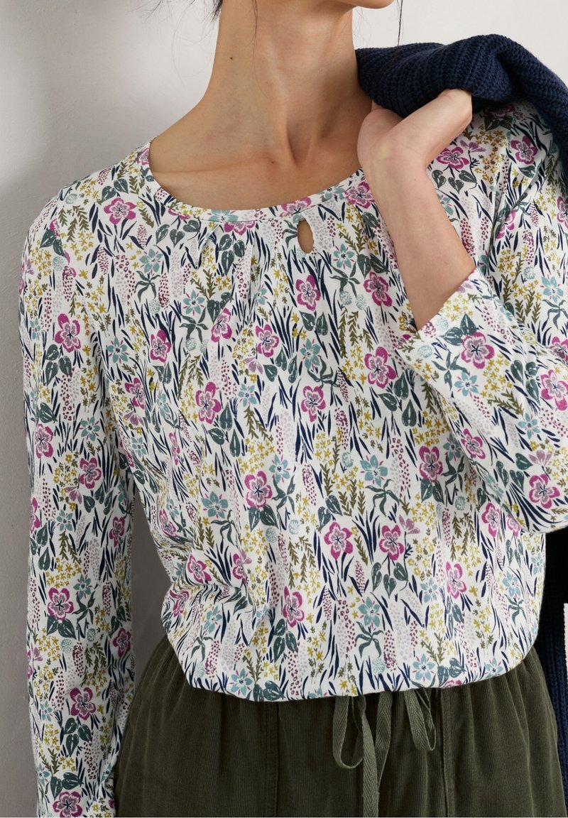 Top a maniche lunghe con motivo floreale in bianco, con fiori rosa e blu, scollo a chiave e vestibilità rilassata, abbinato a pantaloni verde oliva.