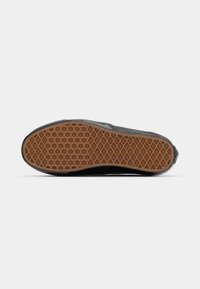 Zwarte sneaker met een gestructureerde rubberen buitenzool met een ruitpatroon. De zool heeft een gumkleur, wat contrasteert met het zwarte ontwerp.
