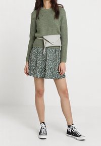 Vihreä ribbineulepaita, kukallinen A-linjainen hame valkoisella ja vihreällä kuviolla, vaaleanharmaa vyölaukku ja mustat korkeavartiset tennarit.