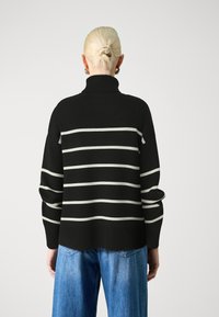Black and white striped sweater with a high neck and loose sleeves, made of a soft knit material. Paired with wide-leg denim jeans.