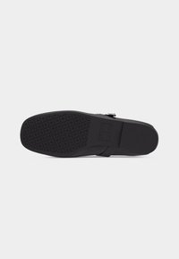 Semelle d'une chaussure formelle noire avec un motif antidérapant texturé sur la moitié avant et une section talon lisse sur un fond clair uni.