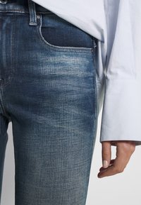 Jeans de mezclilla azul con un sutil degradado de oscuro a claro. Presentan un clásico diseño de cinco bolsillos y una textura suave con costuras visibles.