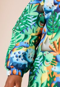 Colorful jacket featuring a playful dinosaur and foliage print. Made of smooth fabric with elastic cuffs and a vibrant, multi-colored design.