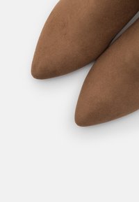 Chaussures en daim marron à bout pointu avec une texture mate, présentant un design épuré et une silhouette effilée, mettant en valeur une finition lisse.