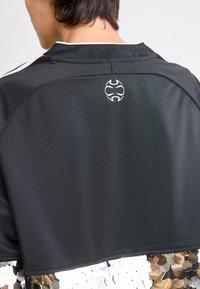 Persona, kas valkā melnu augšu ar baltu logo augšējā aizmugurē un pamanāmu sekvīnu audumu apakšējā malā.
