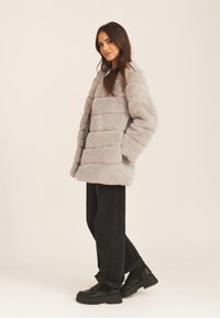 Gray faux fur coat with a boxy design, striped texture, and side pockets, paired with black wide-leg jeans and chunky black boots.