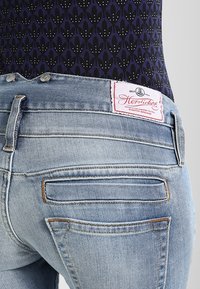 Jeans in denim blu chiaro con vita media, tasche posteriori con cuciture sottili e una toppa in pelle con logo in vita.