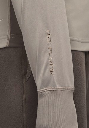 Světle šedé sportovní oblečení s texturovanou tkaninou, s vyšitým nápisem "DRI-FIT" na rukávu a kontrastním tmavě šedým materiálem uvnitř.