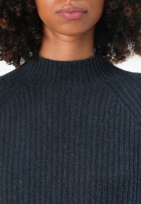 Pulover întunecat cu nervuri, având un guler înalt, un model de tricot texturat și un material moale. Fără branding vizibil sau elemente de design suplimentare.