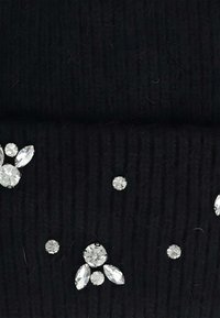 Tessuto nero testurizzato decorato con piccole e medie gemme trasparenti simili a cristalli, disposte in gruppi e singolarmente.