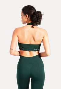 Mörkgrön sport-BH med halterneck-design och XOX-märket. Kombinerad med högmidjade leggings, båda i ett mjukt och stretchigt tyg.