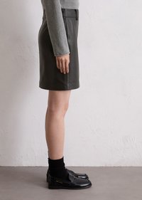 Zwarte leren minirok met een rechte snit en een gladde textuur, gecombineerd met zwarte loafers en geribbelde zwarte sokken.