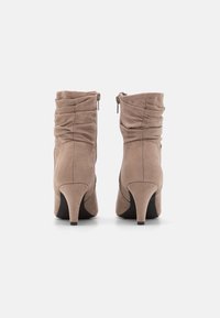 Botines de ante marrón con un diseño arrugado, que presentan un tacón afilado y cremalleras en los lados exteriores, con una textura suave.